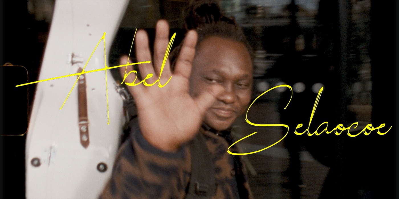 Still from doubleA tapes, episode 1: Abel Selaocoe waving at the camera, his name written across the picture in yellow handwriting