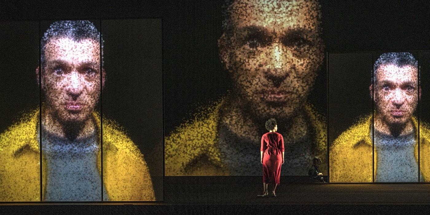 Scene from Upload: a singer in a red dress in front of huge pixelated video faces